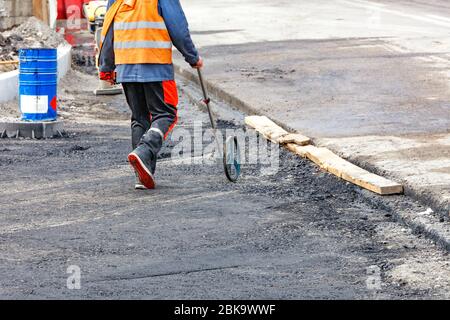 An engineer measuring road distances with a measuring wheel determines the required amount of asphalt for laying on a new section of the road. Stock Photo