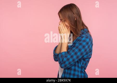 Side view of frustrated girl in checkered shirt holding head down and crying from depression, wiping tears, coping with grief and loss, feeling hopele