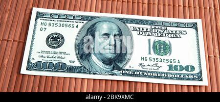 A hundred American dollars bill in close-up on a bambuk mat made of thin brown bamboo sticks. Located slightly on the diagonal. Stock Photo