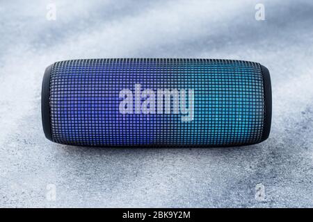 A portable music column on gray grunge concrete background. Musical wireless speaker with blue glow. Sound system Stock Photo