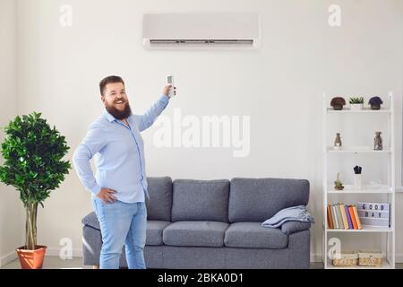 Fat funny man holding an air conditioning control panel at home. Air conditioner. Stock Photo