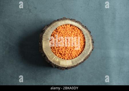 Red lentil in wooden bowl on stone, concrete background. Healthy, organic and delicious raw cereal. Top view, flat lay.