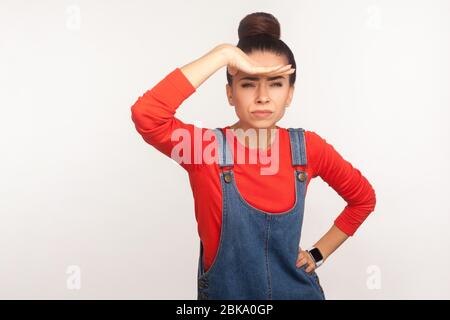 Portrait of girl in denim overalls holding hand over eyes and looking at long distance with confident determined expression, being ambitious about far Stock Photo