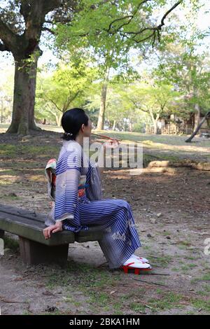 Japanese woman in kimono smoking traditional smoking pipe (kiseru) on a bench in a park Stock Photo