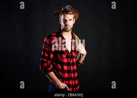 Cowboy wearing hat hold rope. Lasso tool of American cowboy. Still used on ranches to capture cattle or other livestock. Western life. Lassoing on prairie. Man unshaven cowboy black background. Stock Photo