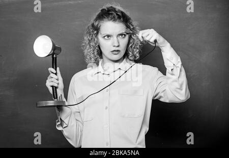 Creativity and inspiration. Teacher hold table lamp in hand chalkboard background. Knowledge day. Light up process of studying. Insight and idea. Educational idea. Woman work on bright shiny idea. Stock Photo