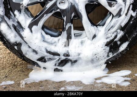 A Part of wheel of car with flow down white foam. Soap water on wheel of washing car, close up view. Stock Photo