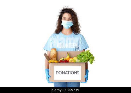 Hispanic girl courier volunteer wear mask hold donation box with food delivery. Stock Photo