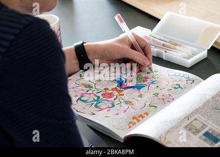A mature middle aged woman colouring in an adult colouring book. A de stressing, calming, mindfulness activity. Patterns are coloured with bright pens Stock Photo
