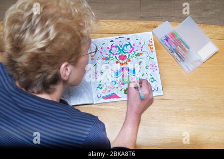 A mature middle aged woman colouring in an adult colouring book. A de stressing, calming, mindfulness activity. Patterns are coloured with bright pens Stock Photo