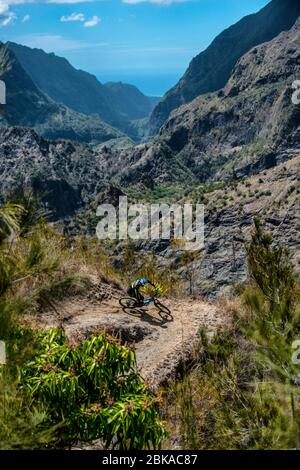 Two men ride mountain bikes down a ridge line trail near the town of Cilaos on Reunion Island in the Indian Ocean. Stock Photo