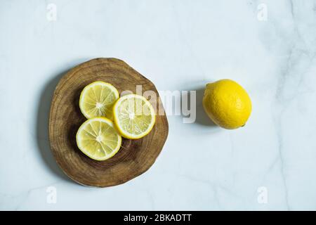 Lemon slices in wooden board with a whole lemon on marble background. Fresh and delicious citrus. Stock Photo