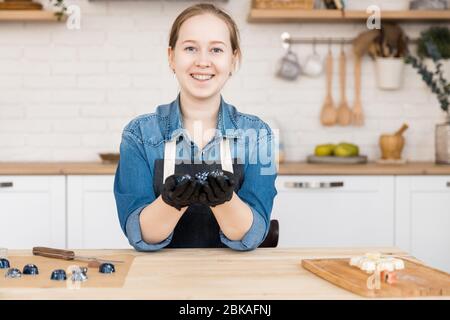 Confectioner holds sweet Belgian chocolate candies on kitchen background. Small business home concept Stock Photo