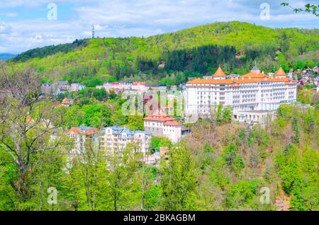 Karlovy Vary Carlsbad historical city centre top aerial view with hotels buildings, Slavkov Forest hills with green trees on slope, blue sky white clouds background, West Bohemia, Czech Republic Stock Photo