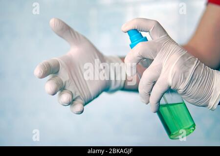 Spray disinfect liquid, hand in white glove on blue background, disinfection at home. Killing germs, bacteria. Antibacterial, antiviral agent in form Stock Photo