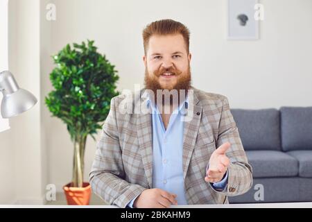 Fat man with a beard looks at the camera talking online using a webcam video chat conference sitting at home office. Stock Photo