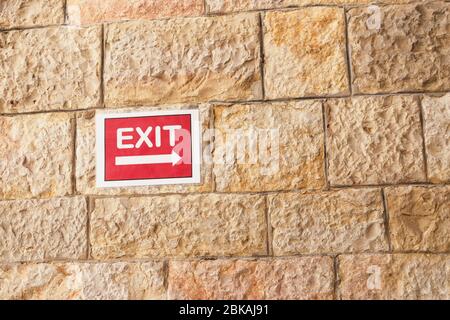 Red exit sign on sandstone textured wall background Stock Photo