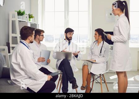 Group of practicing doctors in a meeting discuss the diagnosis of a patient standing in a clinic office. Stock Photo