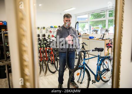 30 April 2020, Hessen, Frankfurt/Main: Christian Theobald, managing director of 'Feine Velos', is standing in his bicycle shop and can be seen in a wall mirror. According to the managing director of 'Feine Velos', sales have been booming since the Corona pandemic. The Corona crisis is currently helping the bicycle to become even more popular as a means of transport for everyday life and leisure. Photo: Andreas Arnold/dpa Stock Photo