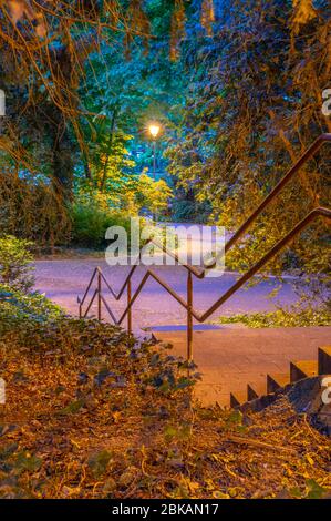 Central city park in Luxembourg City at night when the darkness is falling, shadows are long and streetlamps are already lit Stock Photo
