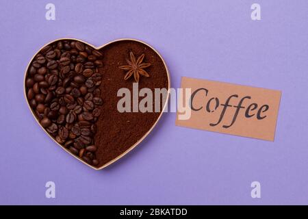 Heart of coffee beans and powder on purple background. Stock Photo