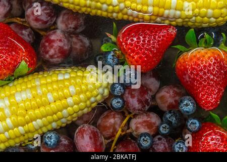 Corn, blueberries, strawberries and grapes floating in water in the sink Stock Photo