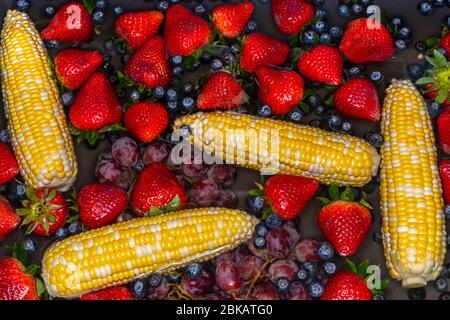 Corn, blueberries, strawberries and grapes floating in water in the sink Stock Photo