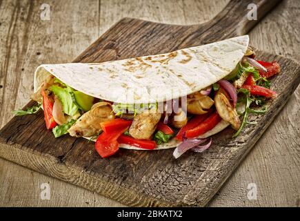 Tortilla wrap with fried chicken meat and vegetables on wooden table Stock Photo