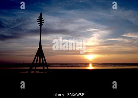 A silhouette of a wooden structure during sunset at Crosby beach, Liverpool with a wind farm in the background on the horizon Stock Photo