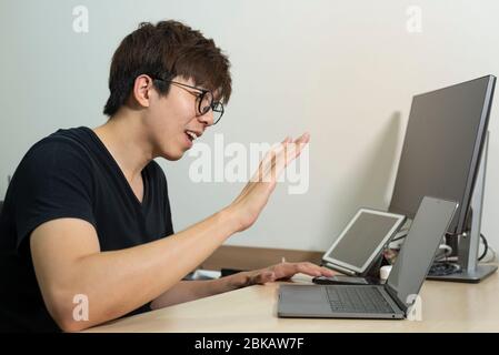 Asian officer man work from home. Man work in action at home. Man with laptop working remotely via high speed internet connection. Communication techn Stock Photo