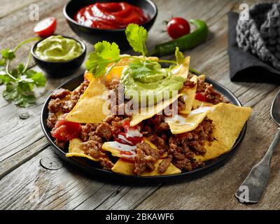 plate of corn chips nachos with fried minced meat and guacamole on wooden kitchen table Stock Photo