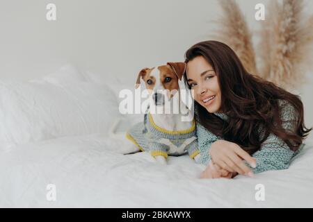 Best friends. Pleased attractive woman lies near jack russell terrier dog, expresses love and care to favorite pet, plays with domestic animal, relax Stock Photo