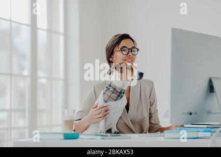 Busy female teacher wears formal clothes and spectacles conducts online lessons for students works at computer poses in coworking space with dog, busy Stock Photo