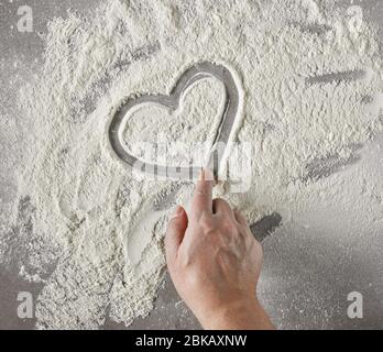 cook hand drawing heart shape in flour on grey table, top view Stock Photo