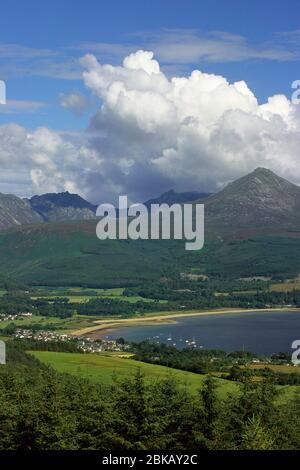 View across Brodick bay to Goatfell with blue sky and big while cumulus clouds over mountain Stock Photo