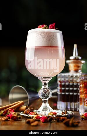 female pink cocktail with foam in a glass. decorated with dried rose. in the background is visible barman inventory Stock Photo