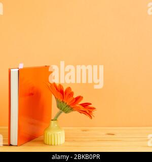 Notebook with orange gerbera flower on wooden table with orange background. Floral arrangement, copy space Stock Photo