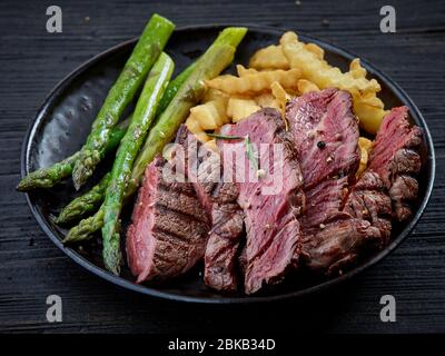plate of grilled beef fillet steak pieces and vegetables on dark wooden table Stock Photo