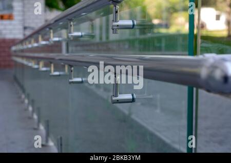 Glass railing for disabled people with chrome handrails. External entrance to the building with an equipped ramp. Close-up. Selective focus. Stock Photo