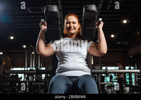 cropped view of purposeful overweight girl doing arms extension exercise on fitness machine Stock Photo