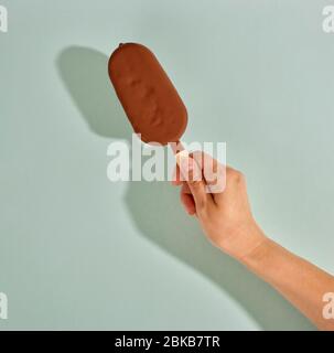 ice cream covered with chocolate isolated on pastel green background in human hand Stock Photo