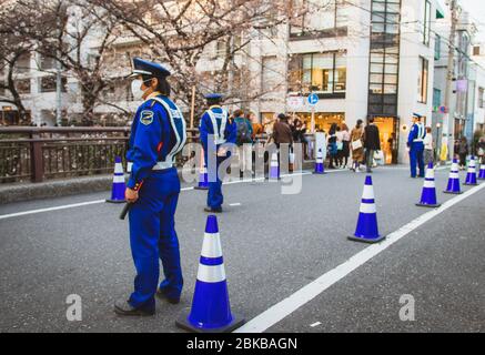 Security guards direct and maintain traffic on a bridge at Meguro River in Tokyo, Japan during the hanami cherry blossom spring season Stock Photo
