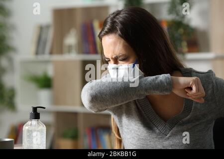 Sick woman with mask coughing on elbow due coronavirus infection at home in the night Stock Photo