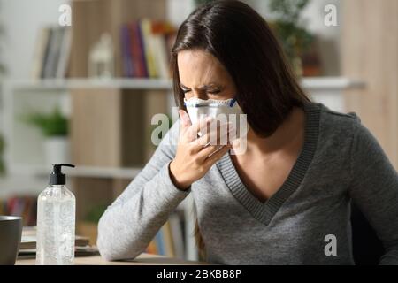 Sick woman coughing with coronavirus symptoms wearing mask sitting on a desk at home in the night