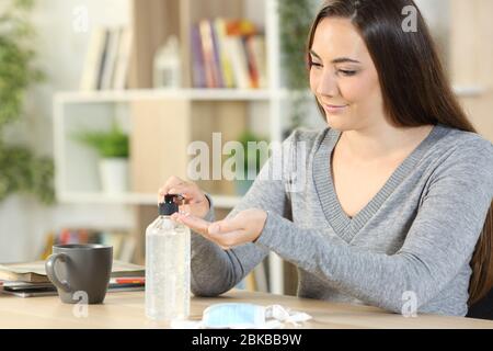 Woman applying hand sanitizer gel from dispenser bottle sitting on a desk at home Stock Photo