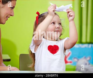 Smiling woman with girl is making origami in the nursery Stock Photo