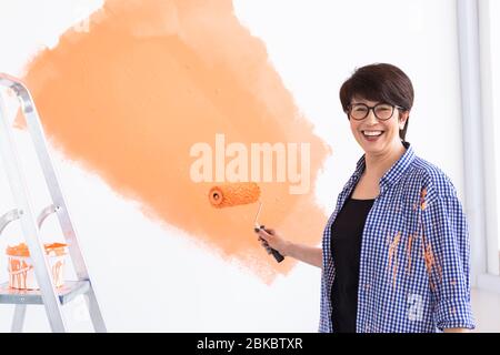 Renovation, redecoration and repair concept - middle-aged woman painting wall in new home. Stock Photo