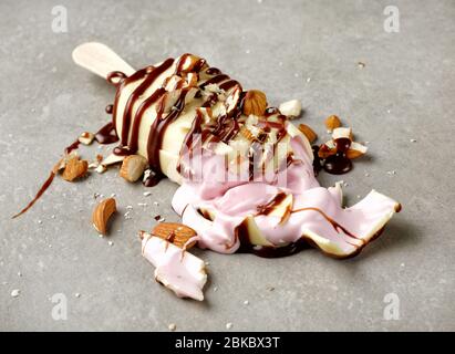 broken ice cream covered with white chocolate decorated with chocolate and almonds on grey plate background Stock Photo