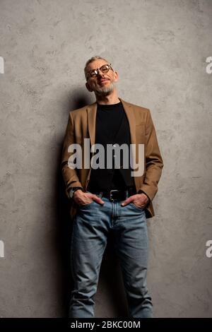 handsome businessman in glasses standing with hands in pockets on grey Stock Photo