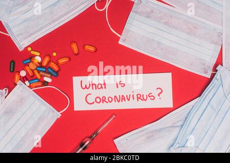 Top view of card with what is coronavirus lettering near medical masks, pills and syringe on red background Stock Photo